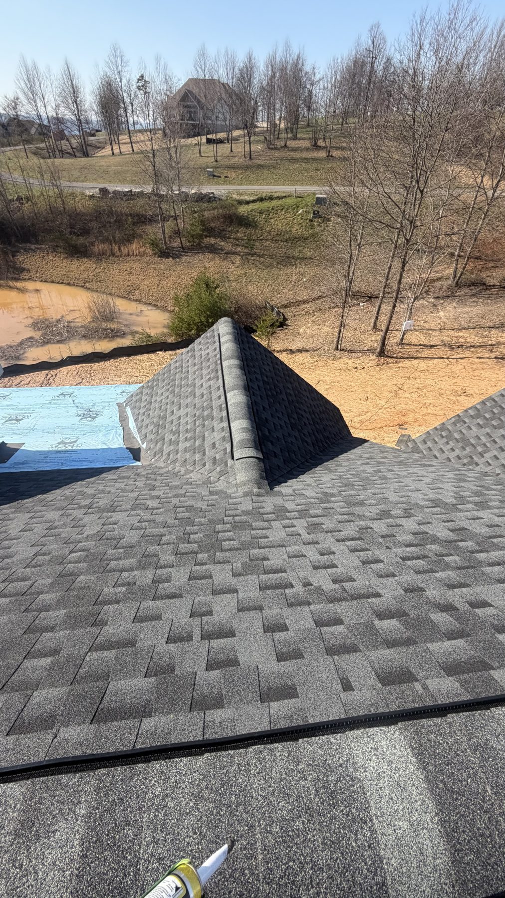 Completed architectural shingle roof with farmhouse visible in the background