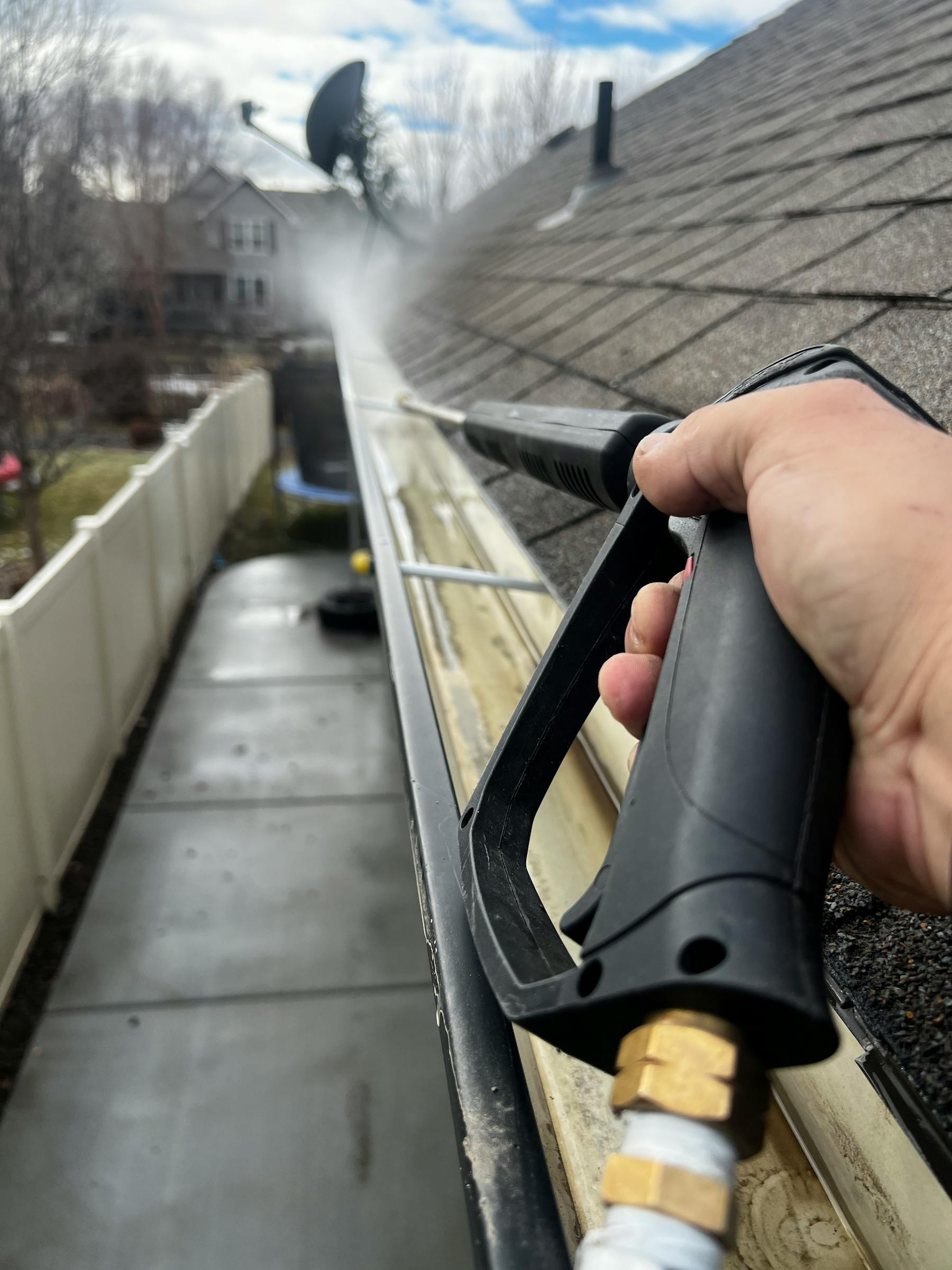 Professional cleaning aluminum house gutter along shingled roofline