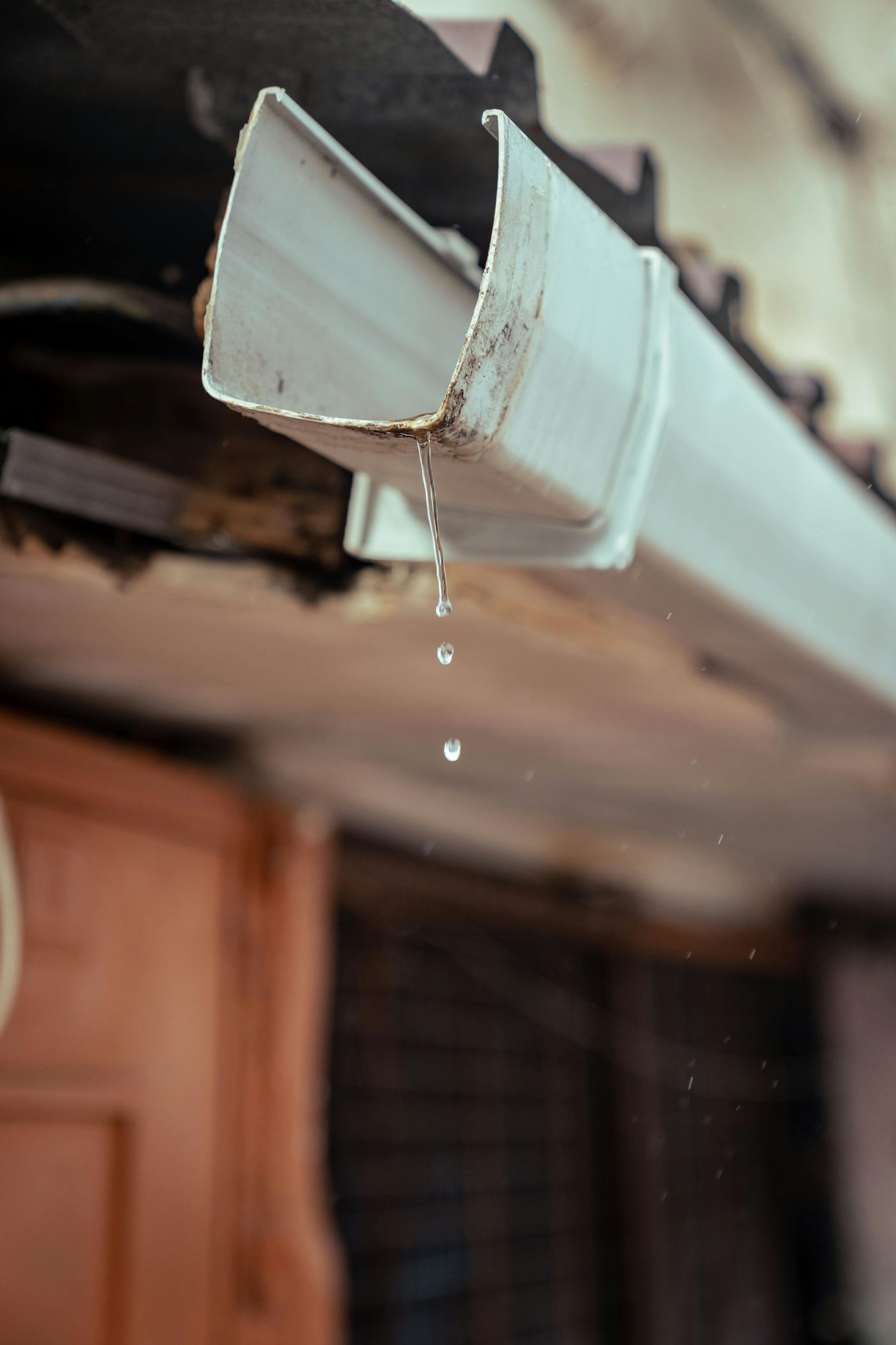Aging white gutter dripping water with visible wear and rust